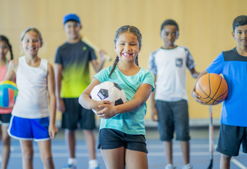 Un groupe d’enfants dans un gymnase tenant du matériel sportif.