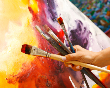 Une main tenant des pinceaux devant un tableau aux couleurs vives.