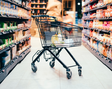 Panier vide dans une allée de supermarché entouré d'étagères remplies de produits.