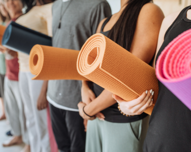 Personnes tenant des tapis de yoga enroulés.