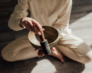 Personne assise tenant un bol chantant en laiton avec un maillet en bois.