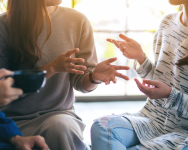 Trois personnes assises et discutant avec des gestes communicatifs.