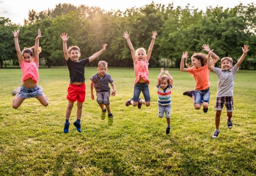 Enfants sautant joyeusement ensemble dans un champ gazonné à l’extérieur.