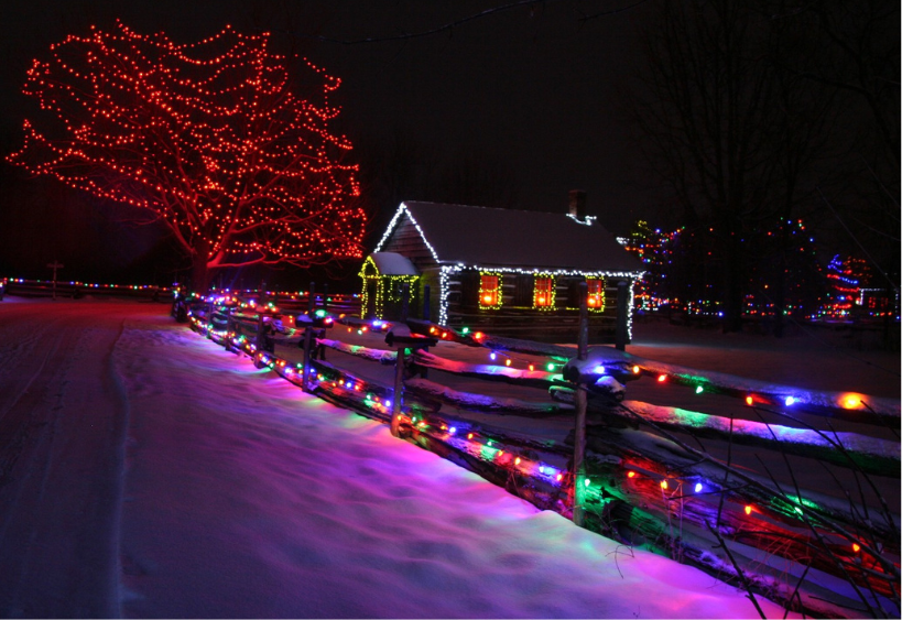 Des guirlandes lumineuses de Noël décorent un chalet enneigé, une clôture et un sapin.