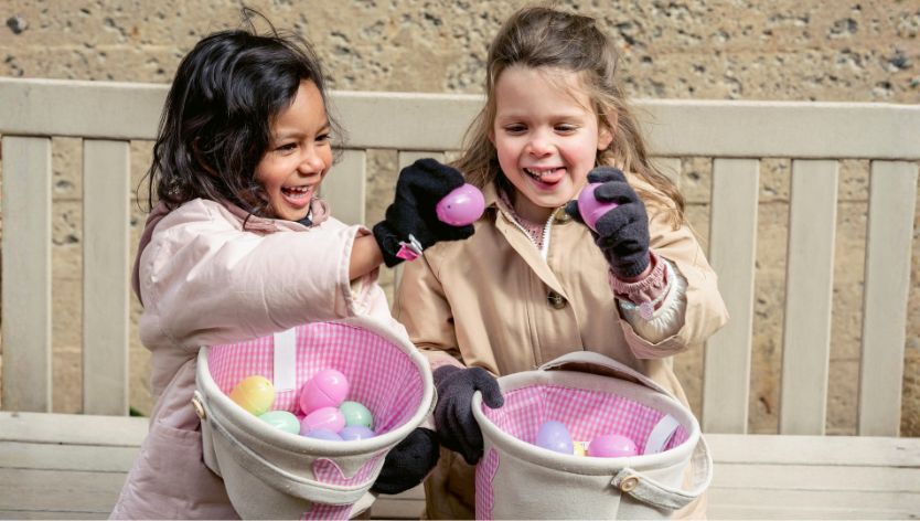 Deux enfants participent à une chasse aux œufs de Pâques en plein air, tenant des œufs colorés et des paniers.