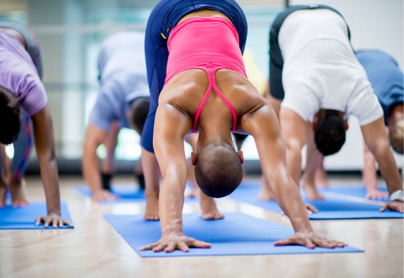 Un groupe d'hommes et de femmes faisant du yoga sur des tapis d'exercice dans un centre de remise en forme.
