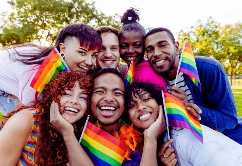Des amis joyeux et multiculturels s’embrassent et rient ensemble tout en brandissant fièrement de petits drapeaux arc-en-ciel