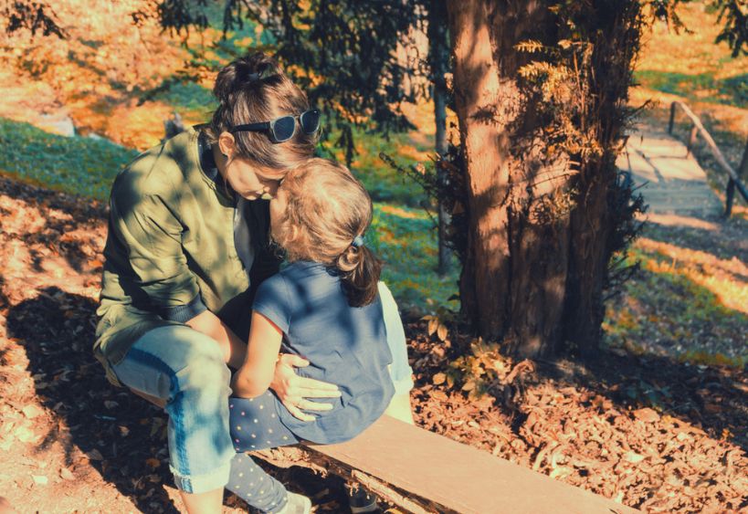 Une mère et sa jeune fille assises face à face sur un banc en pleine nature