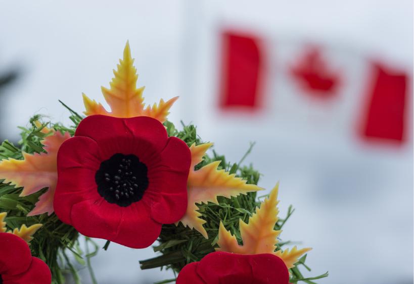Une couronne du Jour du Souvenir entourée de coquelicots, avec un drapeau canadien en arrière-plan