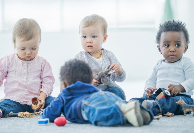 Bébés de 12 à 17 mois assis sur un tapis à l’intérieur, jouant ensemble avec des blocs et des jouets représentant des animaux