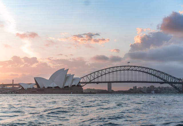 Vue panoramique de l’Opéra de Sydney et du pont du port de Sydney, au coucher du soleil, sur l’eau.