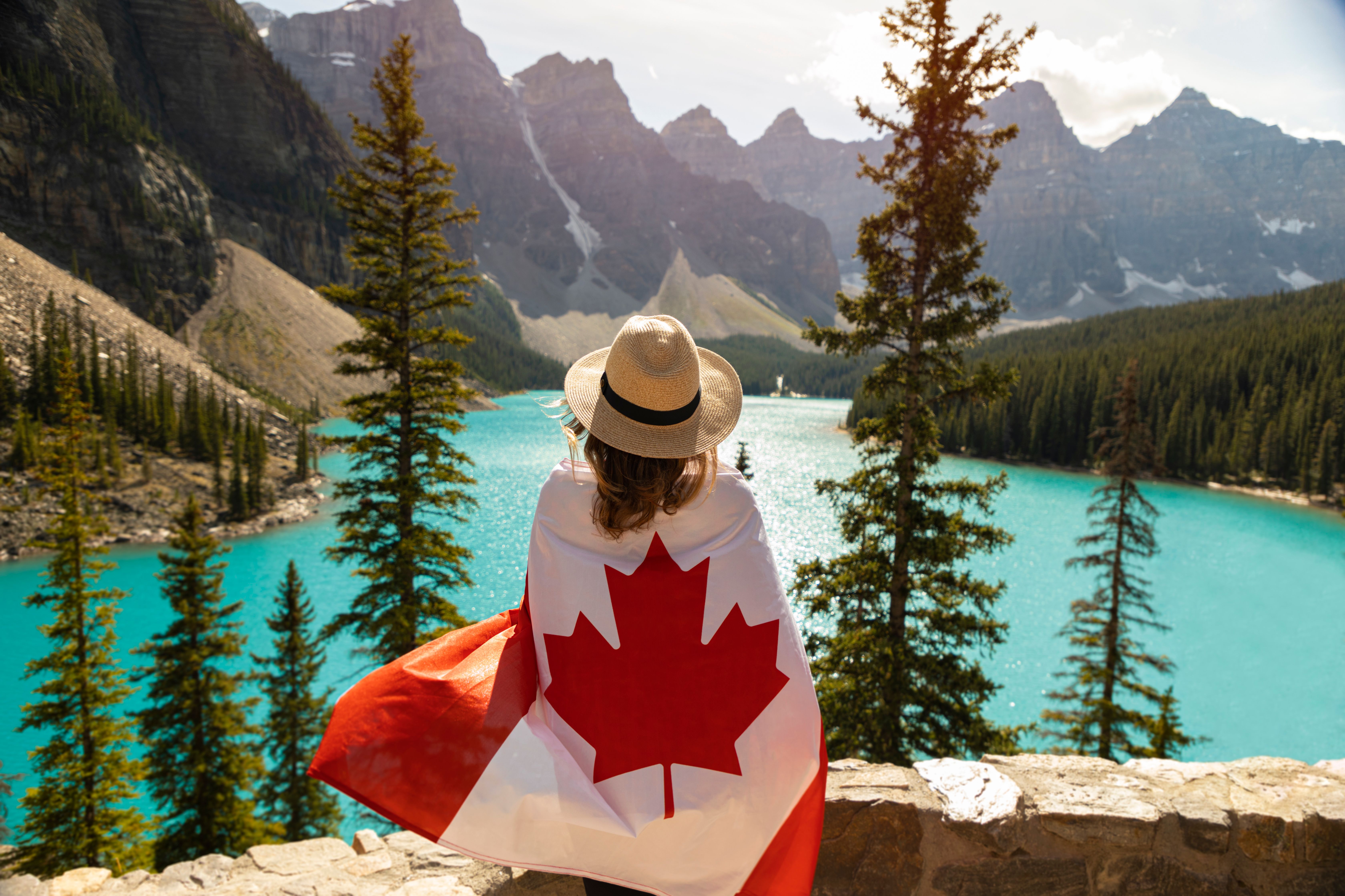 une femme enveloppée dans un drapeau canadien, contemplant un lac niché entre deux montagnes