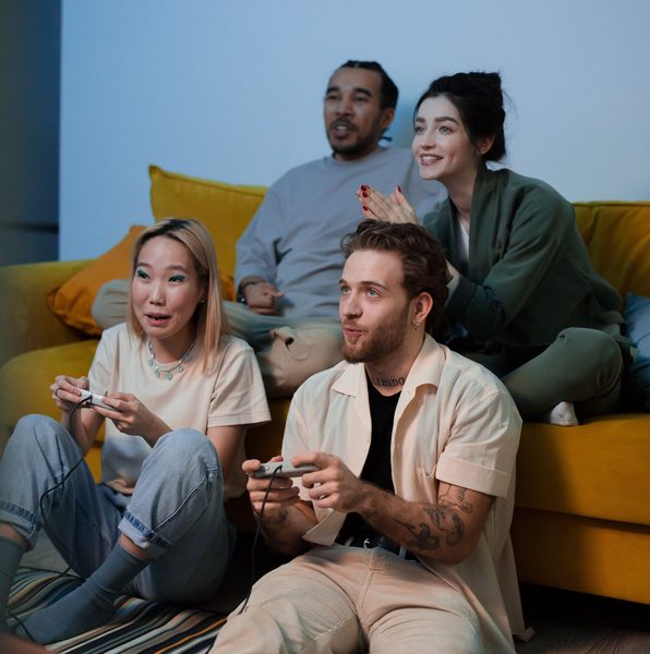 deux personnes qui jouent à des jeux vidéo, tandis que deux autres sont assises derrière elles sur un divan et les regardent