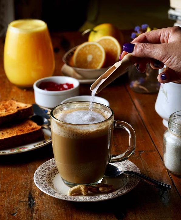 une main versant du sucre dans un café posé sur une table