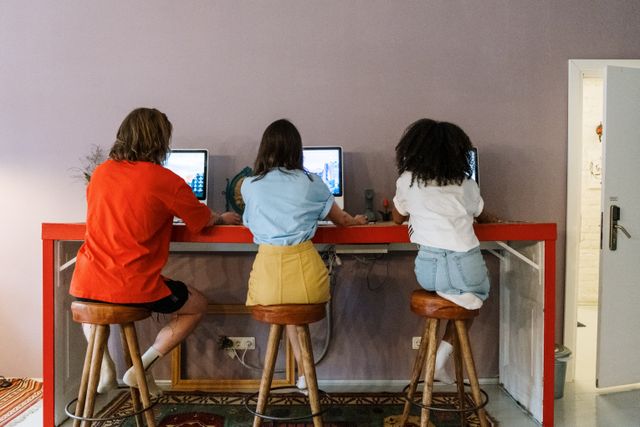 Trois personnes travaillent à un ordinateur dans un espace intérieur moderne, avec des tabourets en bois.