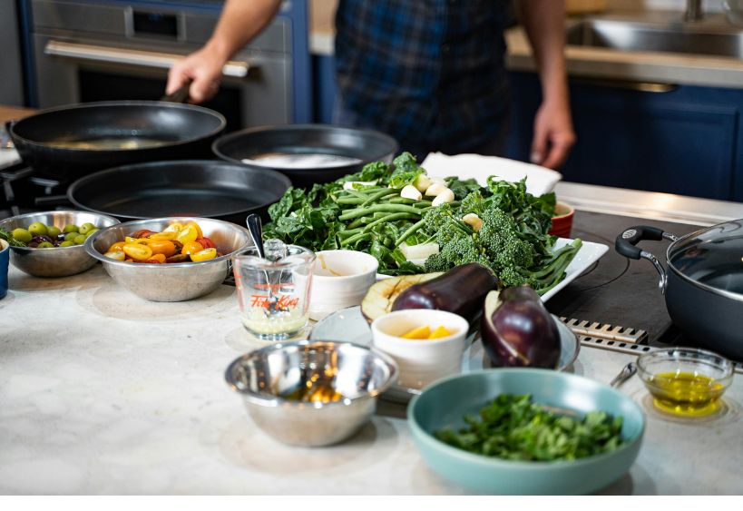 Des ingrédients frais et des ustensiles de cuisine sont disposés sur un comptoir, prêts pour la préparation d’un repas.