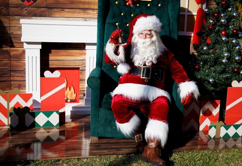 Le Père Noël est assis dans un grand fauteuil et fait tinter une cloche.