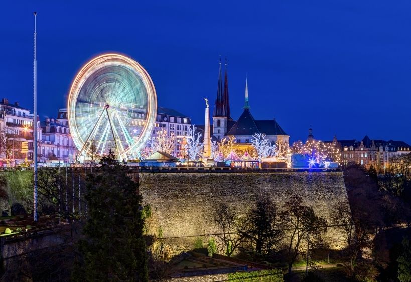 Une grande roue illuminée domine un marché de Noël festif au coeur d'une ville historique.
