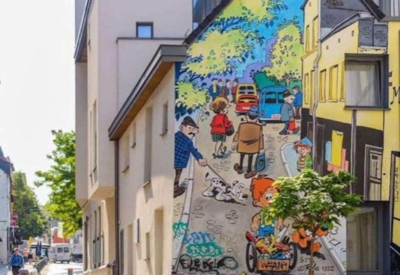 Une murale colorée de bande dessinée orne le mur d’un bâtiment le long d’une rue urbaine.