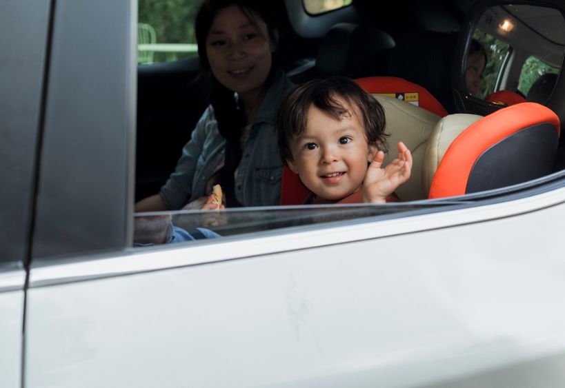 enfant en bas âge faisant un signe de la main depuis une voiture