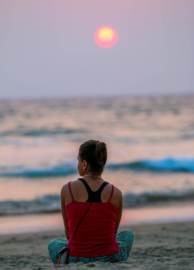 Une femme en débardeur rouge assise sur la plage au coucher du soleil