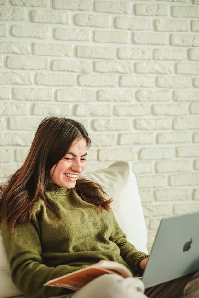 Femme avec un ordinateur portable et un livre assise dans le salon