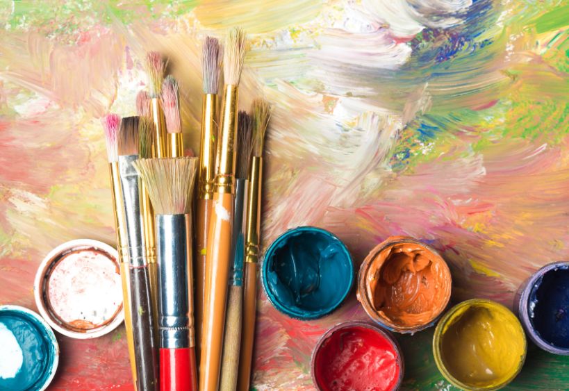 Des pinceaux et des pots de peinture posés sur une peinture abstraite et colorée.