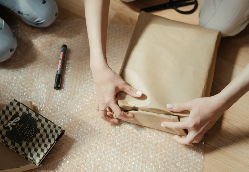 a person wrapping a box in brown paper with marker and bubble wrap on the floor next to them