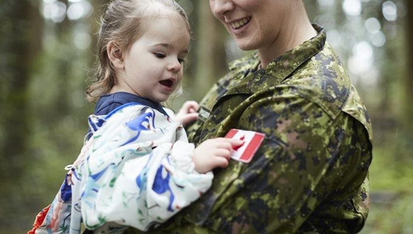 a smiling mother in military uniform holds her young daughter
