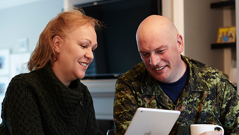 Un couple de militaires, souriant, prenant un café tout en regardant une tablette
