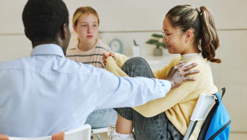 Trois jeunes assis en rond, l'un tendant une main de soutien à l'autre