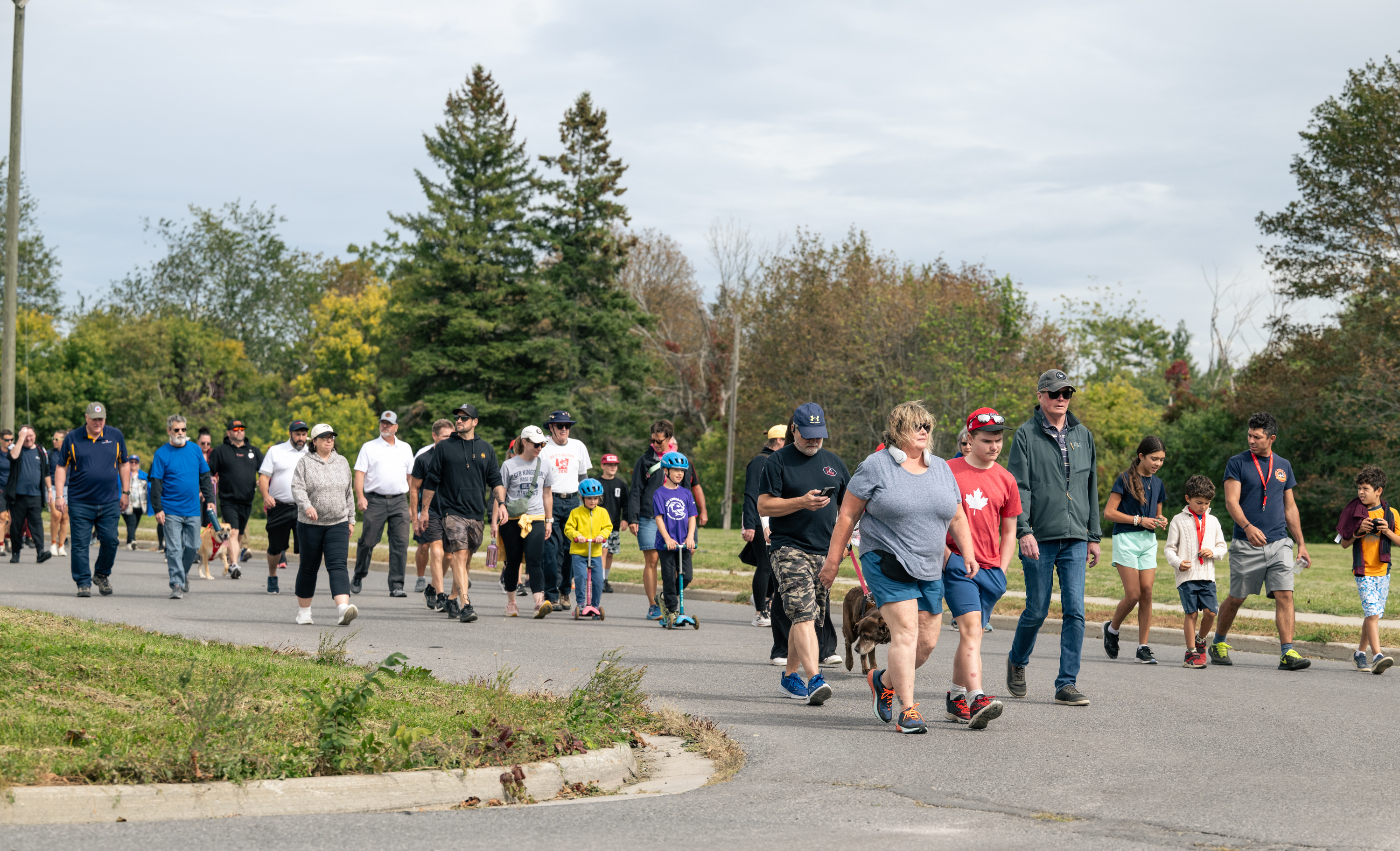 A large group of adults and children walking together along a paved road during the Canadian Walk for Veterans in Kingston. Participants of different ages, including families and community members, ta