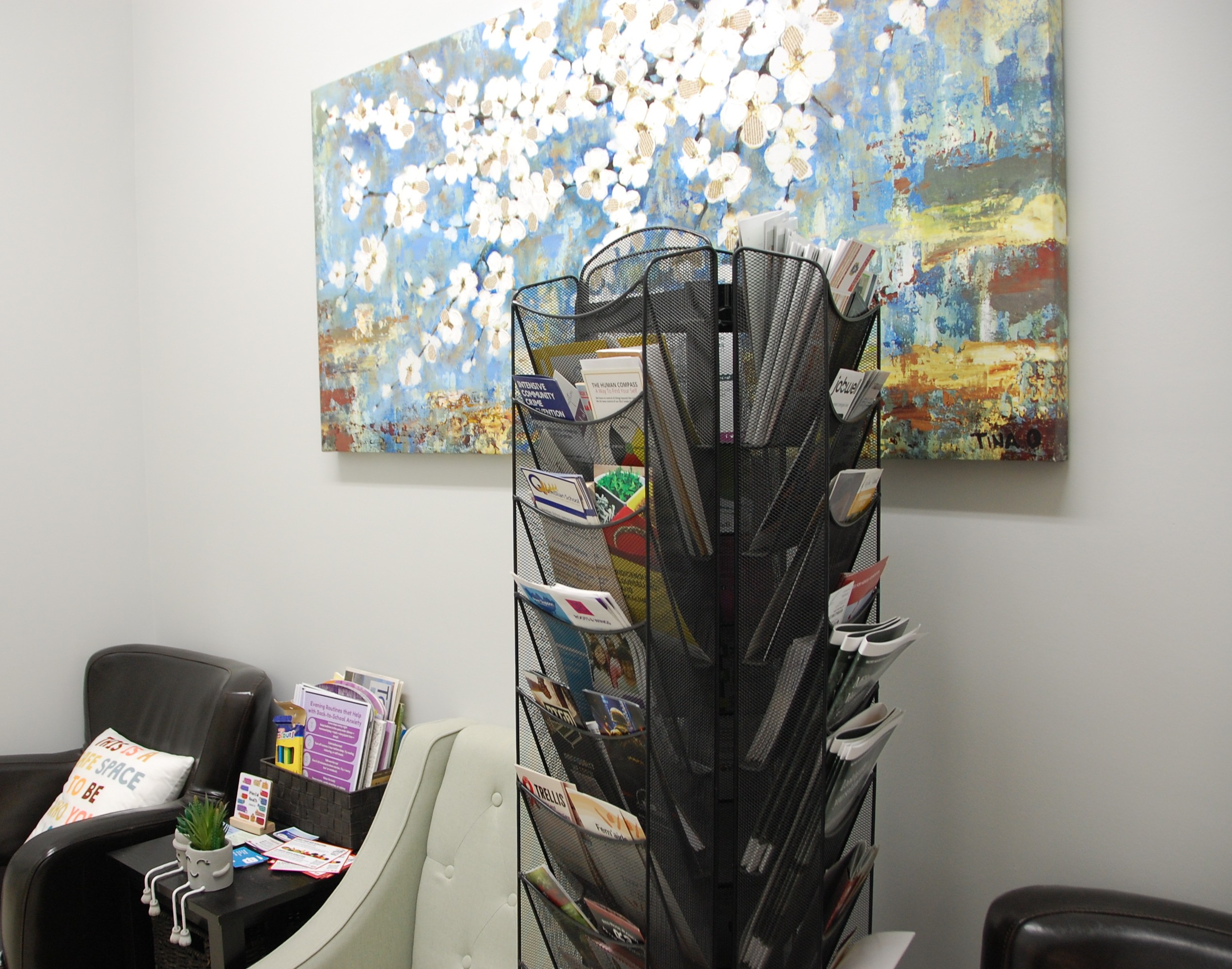 Salle d’attente lumineuse et accueillante pour les services de santé mentale, avec des fauteuils confortables, une petite table avec des brochures, un présentoir rotatif rempli de ressources communaut