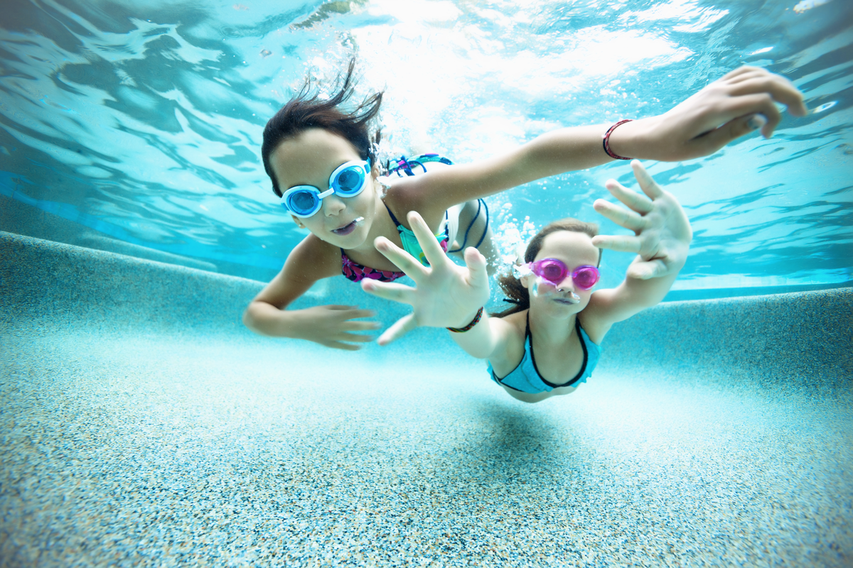 Une photo sous l’eau de deux enfants portant des lunettes de natation et en train de nager.