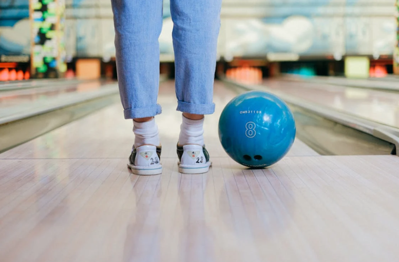 Une personne se tenant à la fin d'une piste de bowling avec une boule de bowling bleue à côté d'elle