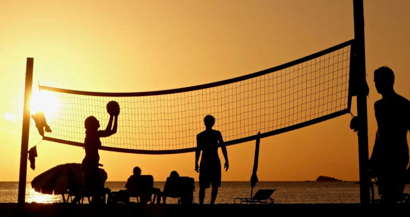 Des gens jouent au volleyball de plage au coucher du soleil